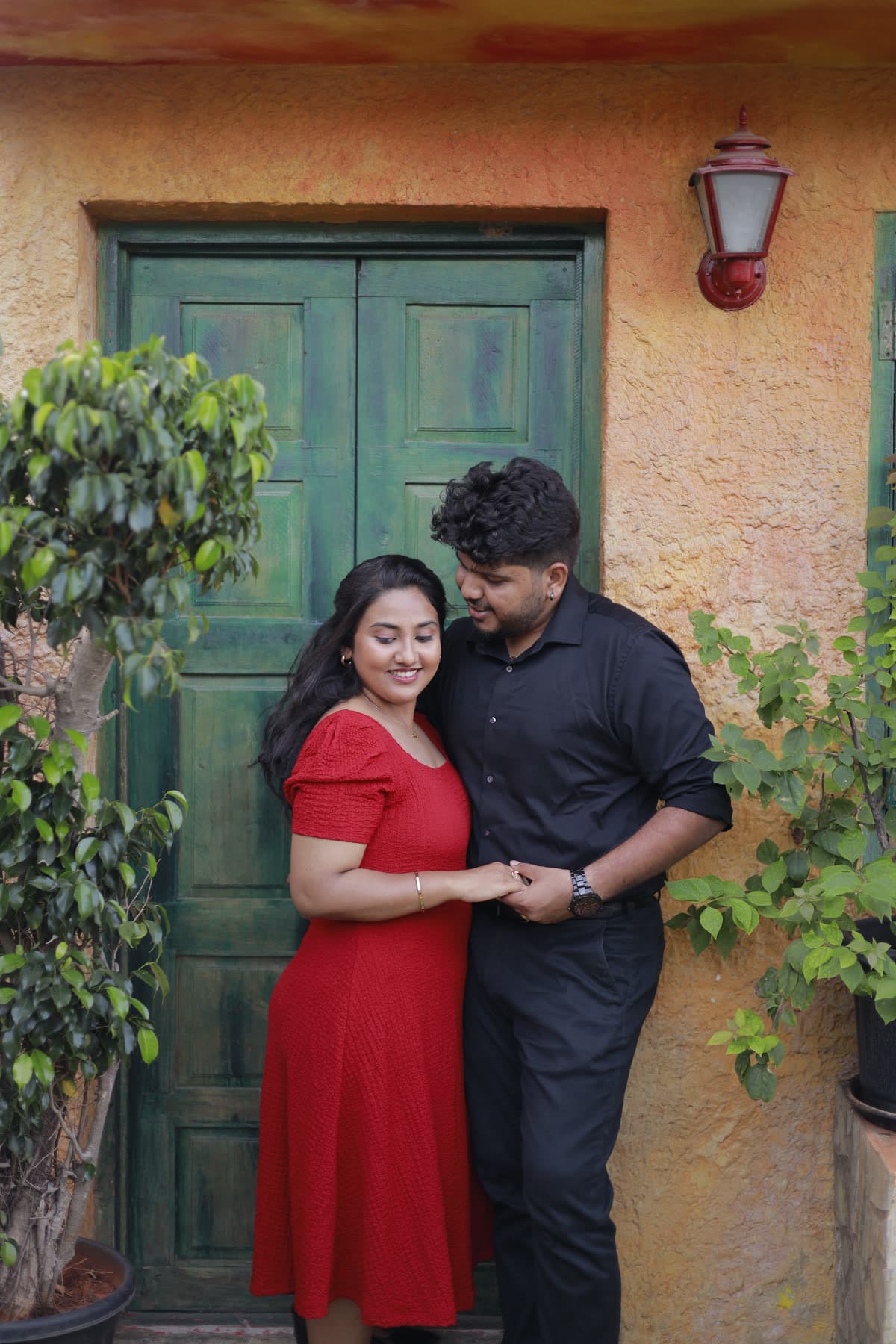 Couple standing beside a weathered green wooden door framed by flowers
