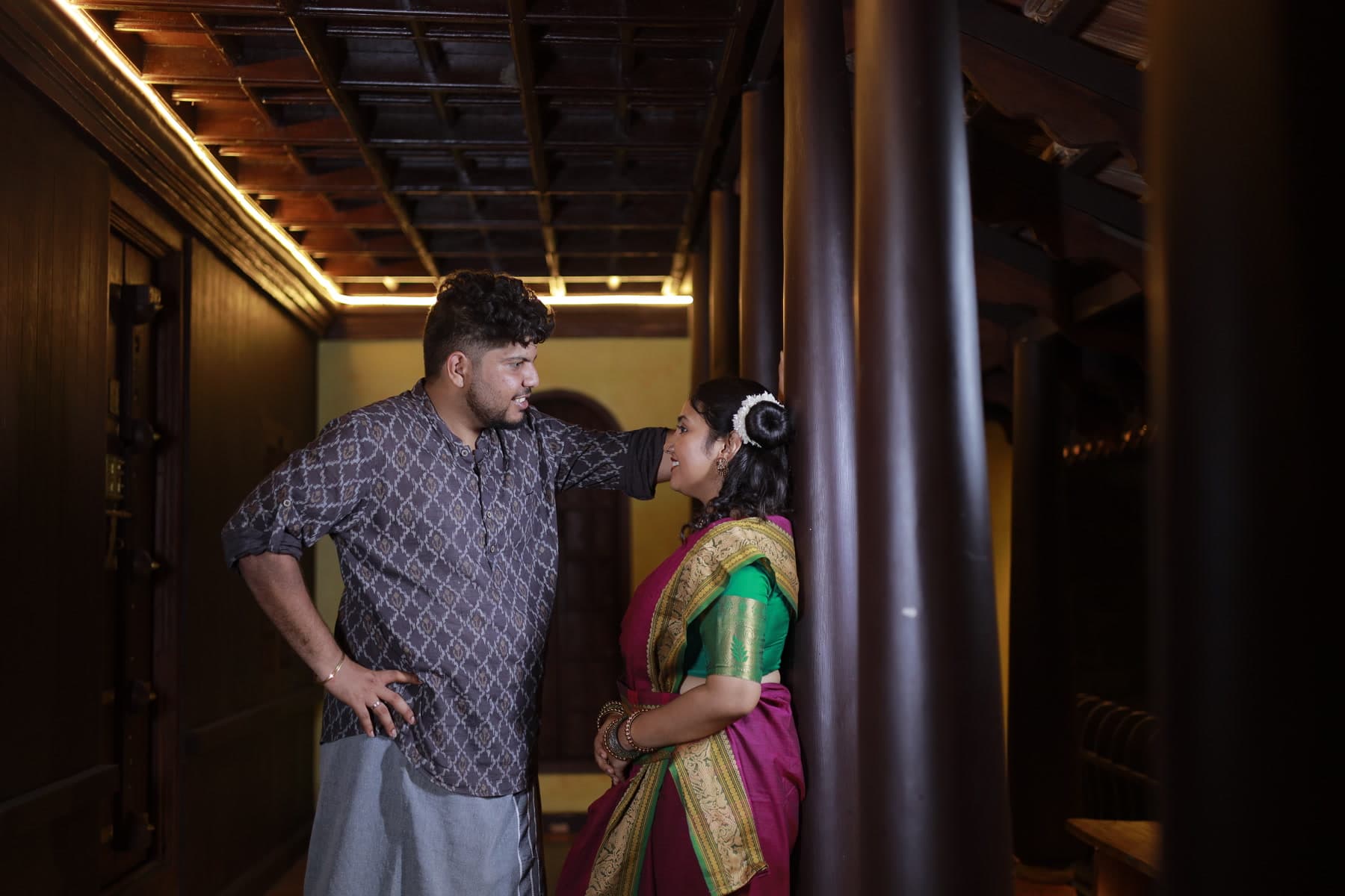 Two people standing in a wooden pillared corridor with carved ceiling beams